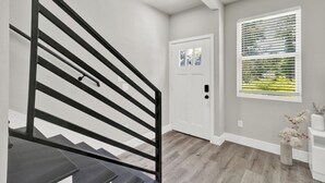 A staircase with a black railing leading to a door, a window with blinds, and a vase with flowers on a pedestal. - Pet-Friendly 3BR/3BA • 15 Min to Airport (Humble)