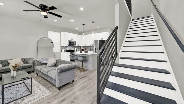 A modern living room with a grey sofa, a coffee table, and a staircase with black railings. - Pet-Friendly 3BR/3BA • 15 Min to Airport (Humble)