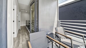 A modern balcony with a glass table and chairs, a metal railing, and a view of the building's interior. - Pet-Friendly 3BR/3BA • 15 Min to Airport (Humble)