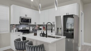 A modern kitchen with white cabinets, stainless steel appliances, and a central island with bar stools. - Pet-Friendly 3BR/3BA • 15 Min to Airport (Humble)