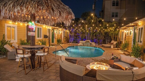 Un área junto a la piscina con techo de paja, asientos de bar y sillas de descanso.