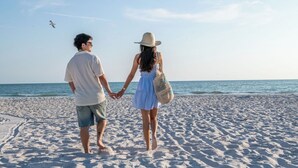 Una pareja tomados de la mano en una playa arenosa, con el océano al fondo.