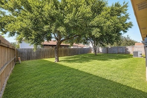 A backyard with a wooden fence, a tree, and a grassy lawn. - Covered Patio + Grill • Backyard • 2Mi to Basilica (San Juan)
