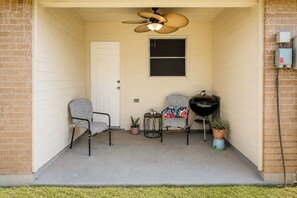 A porch with two chairs, a small table, a grill, and a ceiling fan. - Covered Patio + Grill • Backyard • 2Mi to Basilica (San Juan)