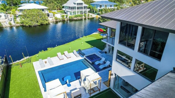 A modern house with a large pool, a tennis court, and a view of the water.