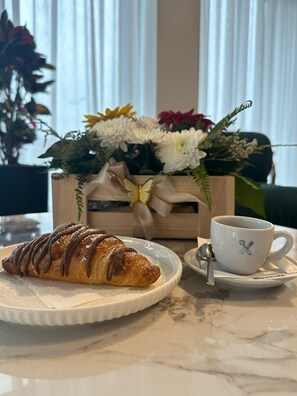 A croissant on a plate, a cup with a spoon, and a bouquet of flowers on a table.