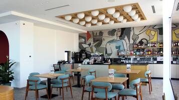 A restaurant with wooden tables and chairs, a bar area with shelves of bottles, and a mural on the wall.