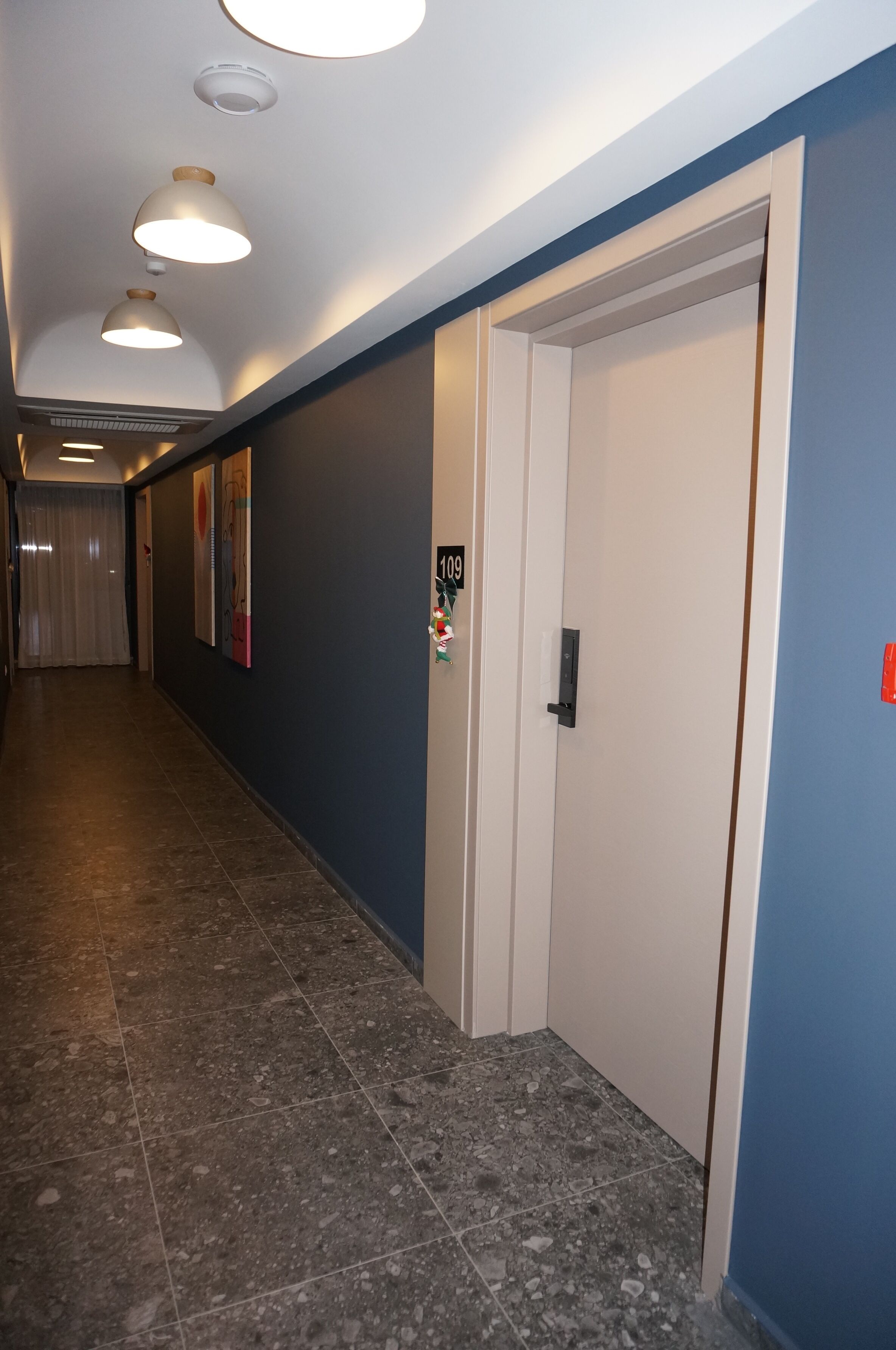 A hallway with a door, a light fixture, and a wall with a number sign.