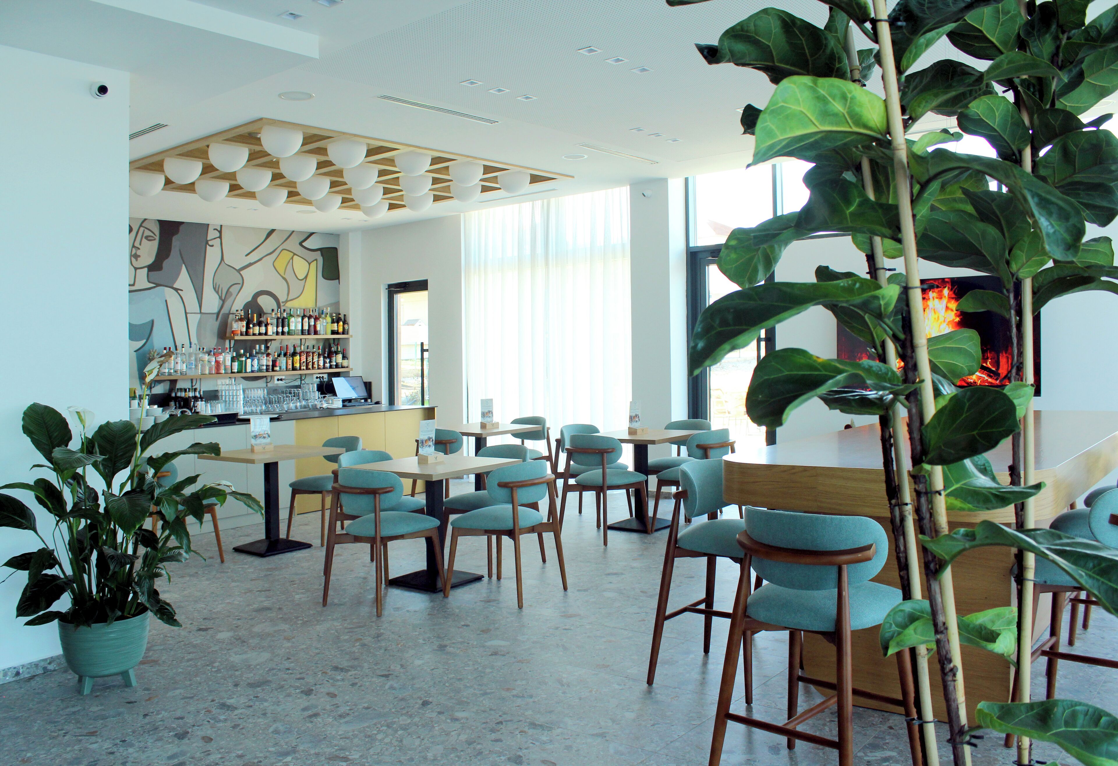Um restaurante moderno com área de bar, diversas opções de assento e amplas janelas que permitem a entrada de luz natural.
