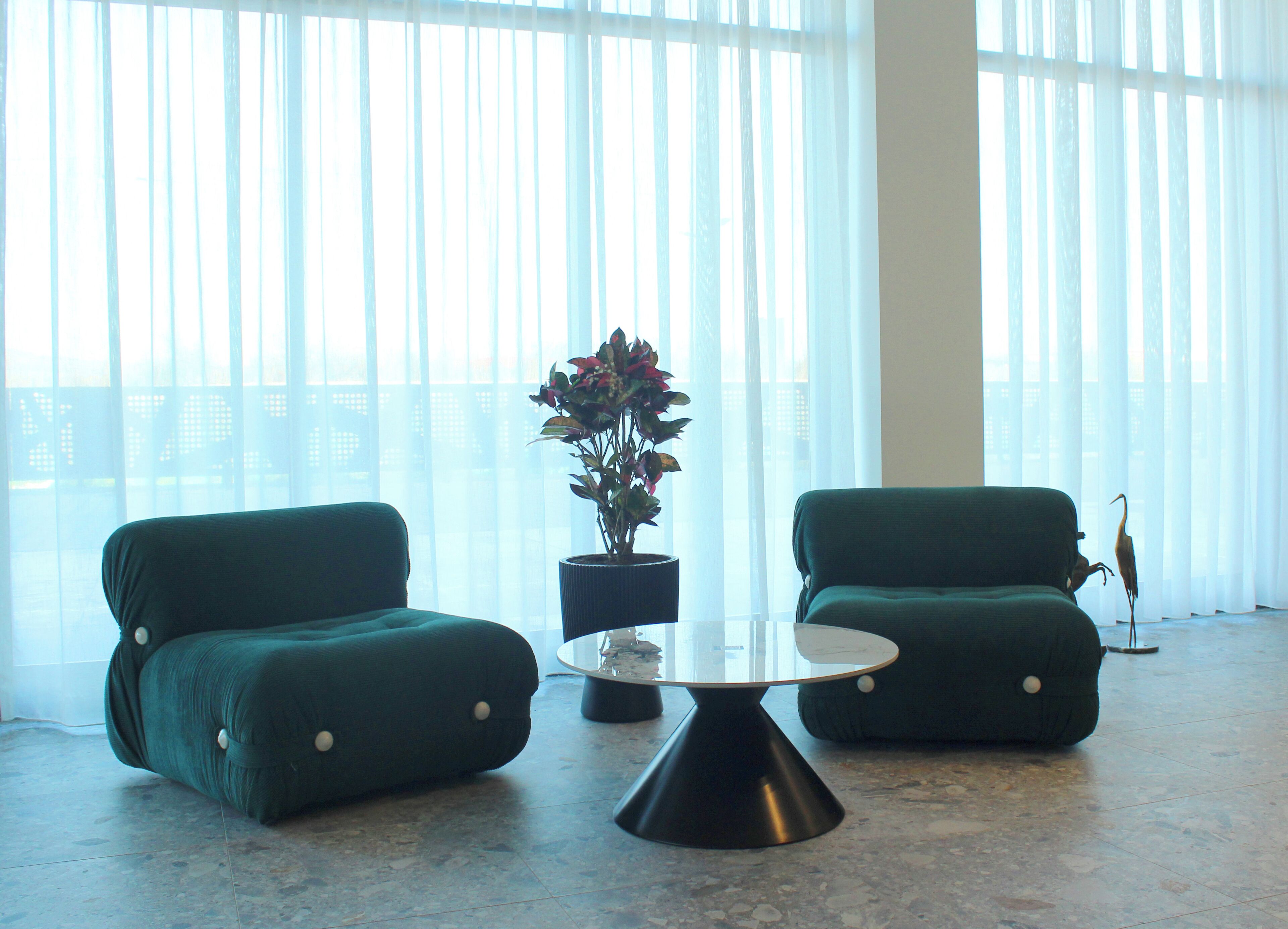 Een moderne kamer met twee groene banken, een ronde tafel en een potplant.