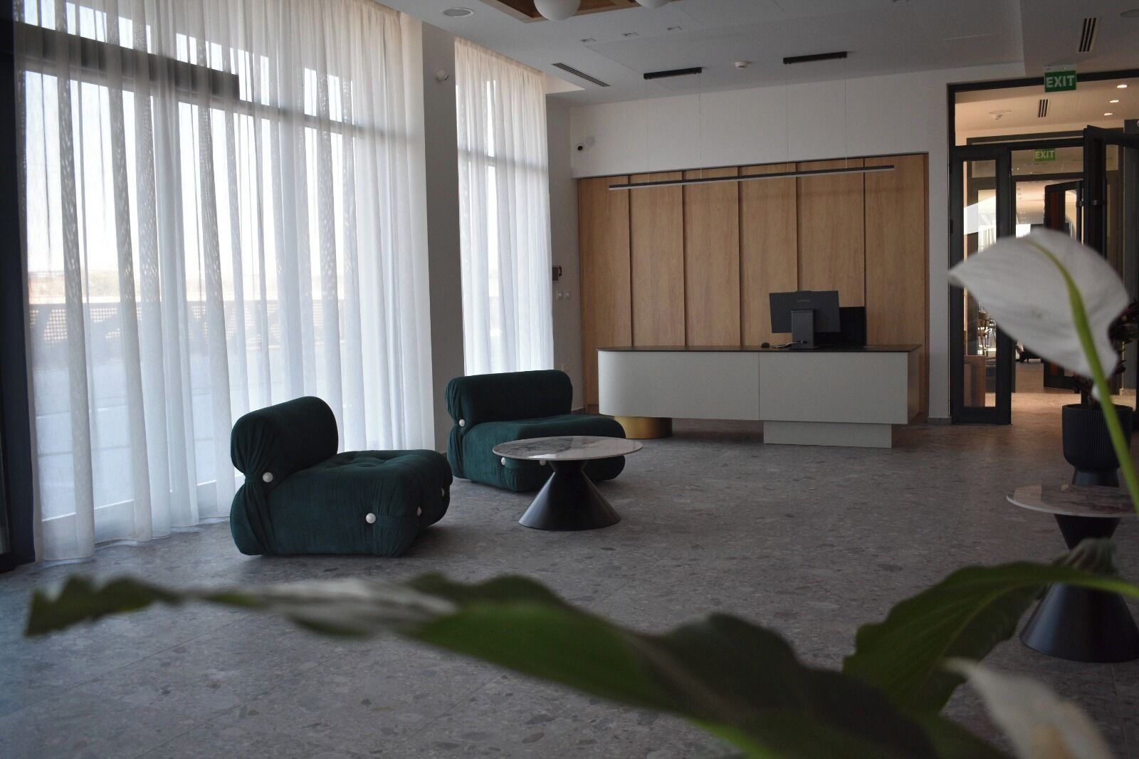 Un lobby moderno con dos sillones verdes, una mesa redonda para café y un mostrador de recepción.
