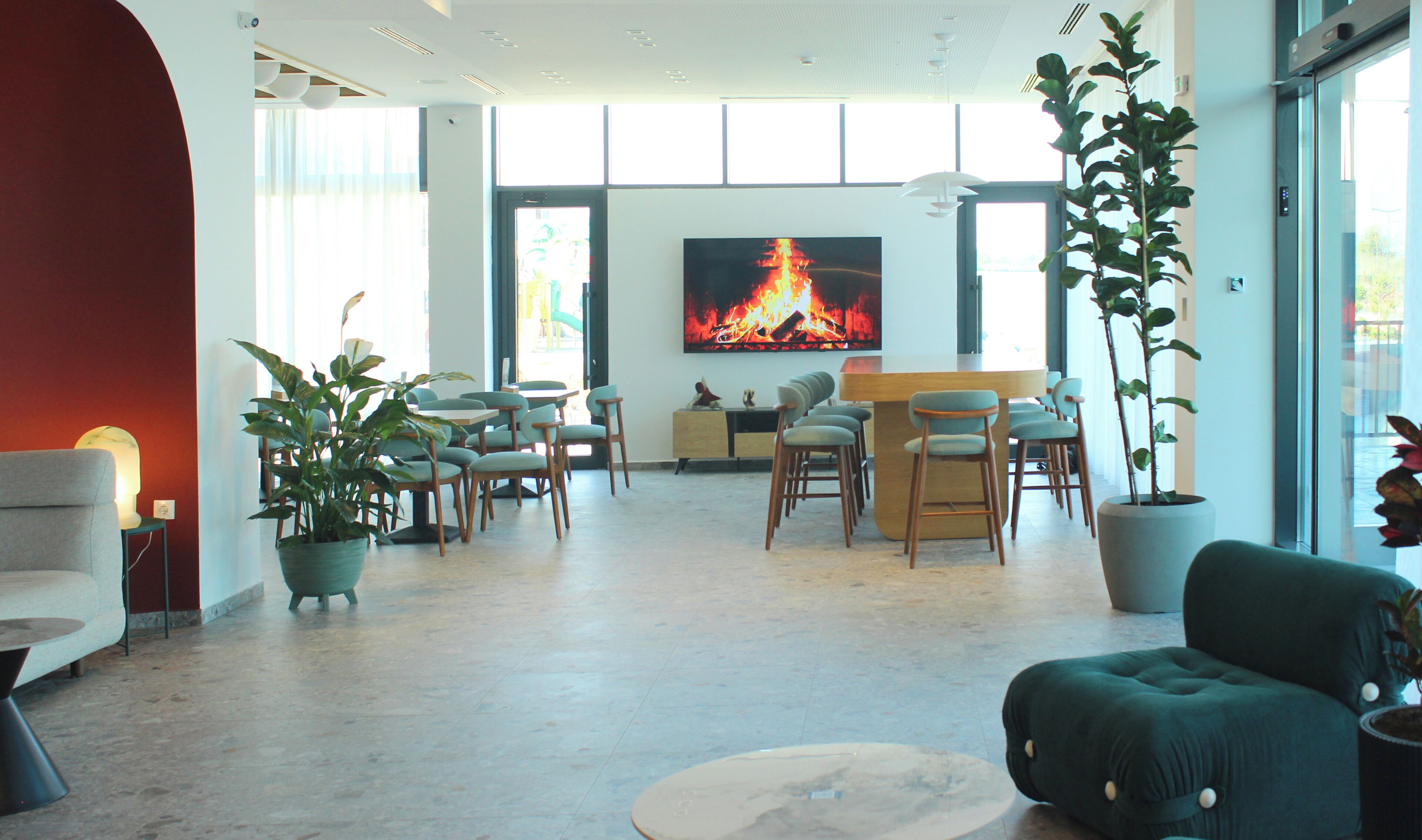 Amplia sala de estar con una pantalla grande mostrando un fuego, asientos cómodos y plantas en macetas.