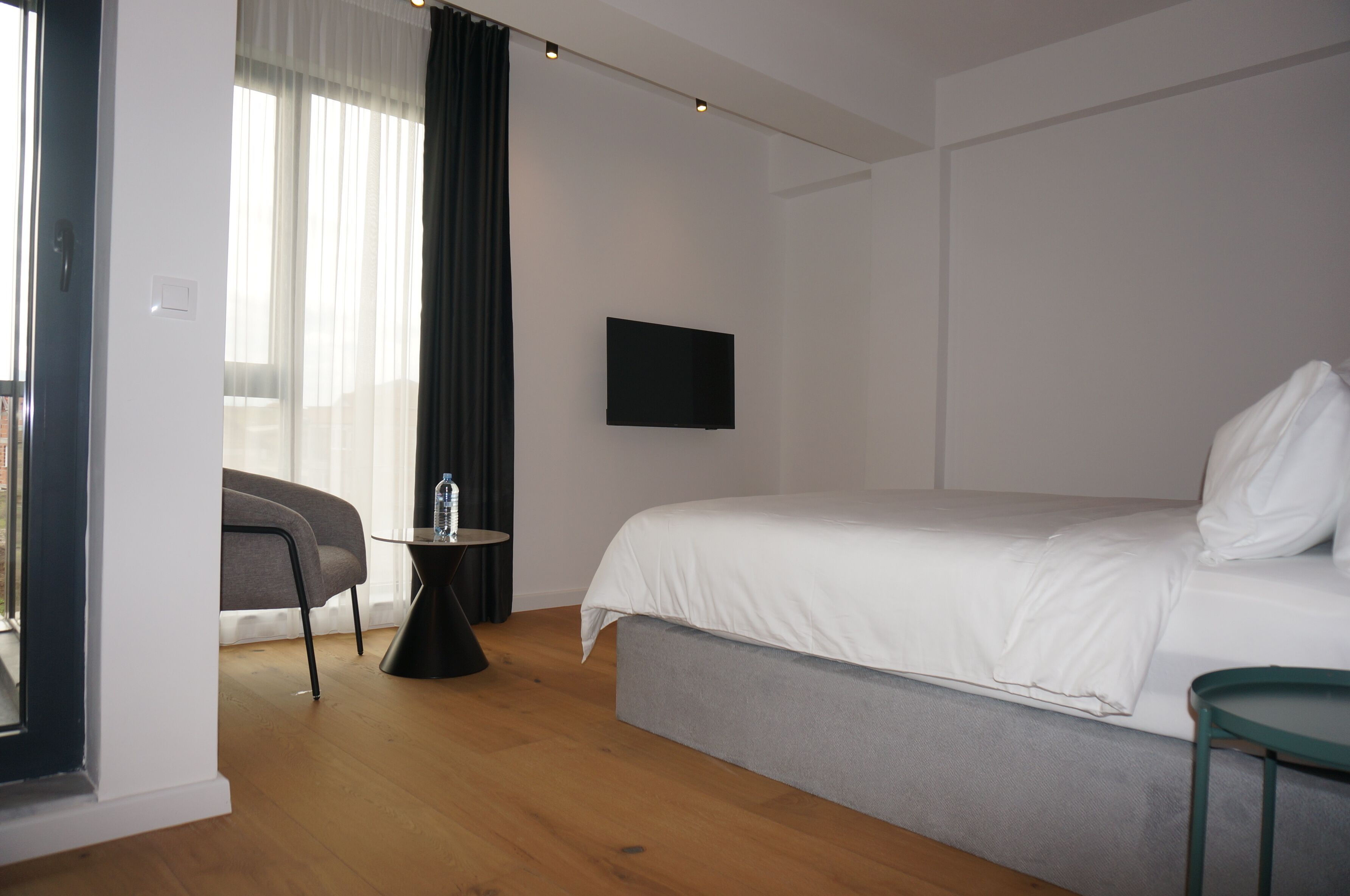 A modern hotel room with a large bed, a flat-screen TV, a small table, and a chair.