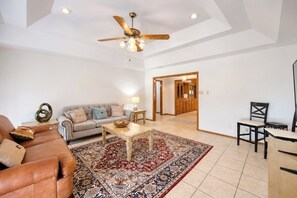 Un salon spacieux avec un plafond haut, un ventilateur de plafond, une grande moquette, un canapé, une table basse et un coin repas avec des chaises.