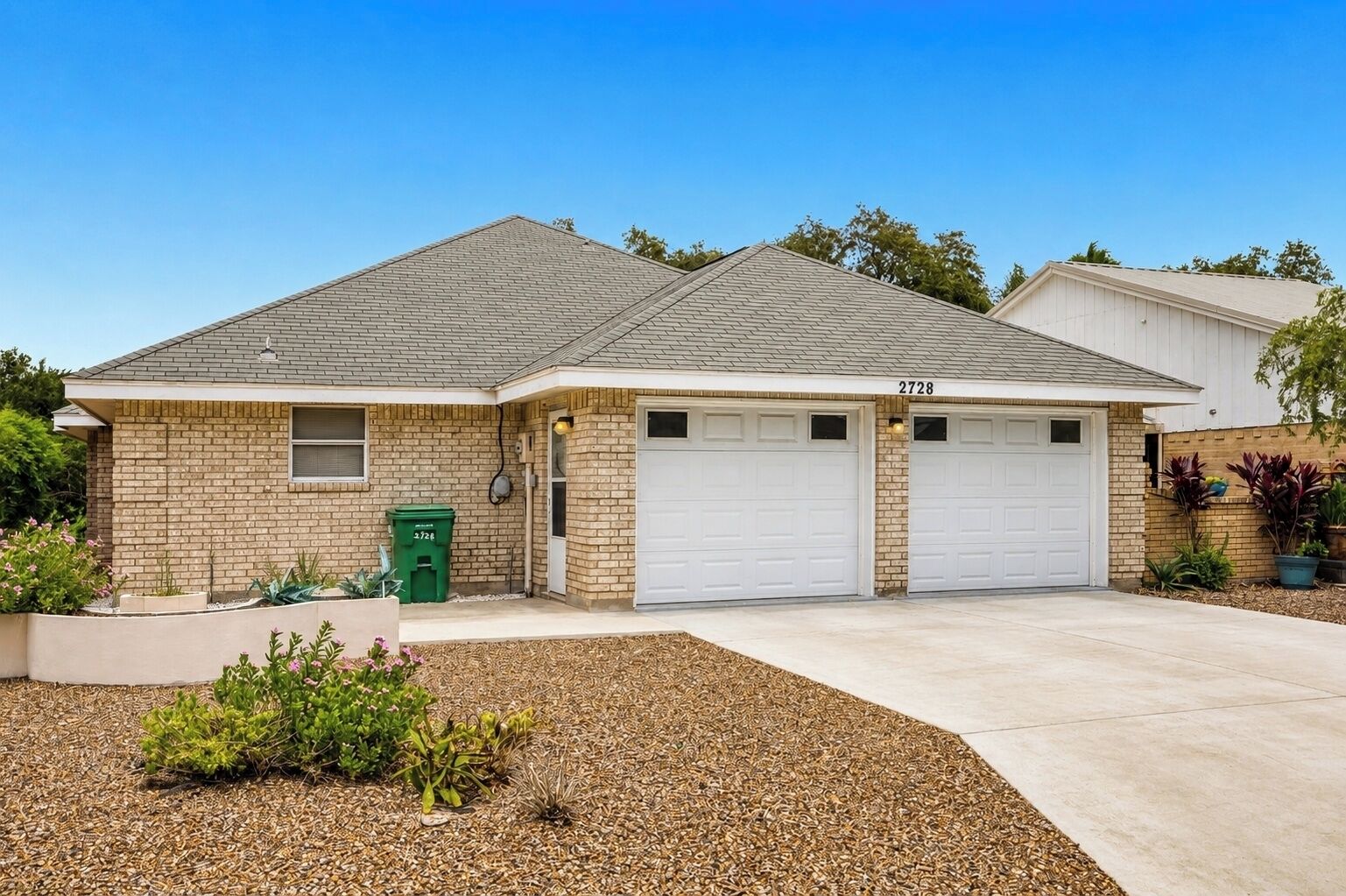 A two-story house with a brick exterior, two garage doors, and a driveway leading to the front entrance.