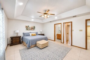 Ein Schlafzimmer mit einem Bett, Nachttischen, einem Deckenventilator, einem Teppich und einem durch eine offene Tür einsehbaren Badezimmer.