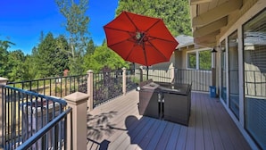 A wooden deck with a red umbrella, outdoor furniture, and a view of trees and a car in the background. - Outdoor Deck • Disc/Pool Table • Fireplace • Grill (Camino)