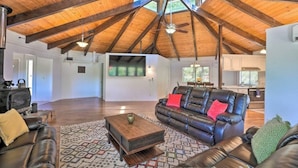 A spacious living area with a high ceiling, a leather sofa, a wooden coffee table, and a patterned rug. - Outdoor Deck • Disc/Pool Table • Fireplace • Grill (Camino)