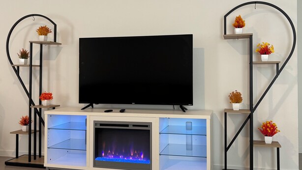Un'elegante mobile soggiorno moderno con TV a schermo piatto, camino a incasso ed mensole decorate con fiori.