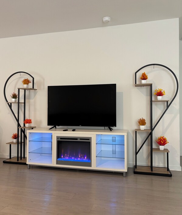 A modern entertainment unit with a flat-screen TV, built-in fireplace, and decorative shelves with flowers. - New Home in New Community Near Downtown Houston (Houston)