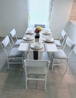 A dining table set for eight with white plates and bowls, surrounded by grey upholstered chairs. - New Home in New Community Near Downtown Houston (Houston)