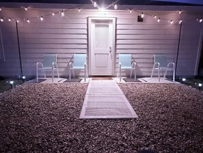 A pathway leading to a door with two chairs on either side, surrounded by gravel and string lights. - New Home in New Community Near Downtown Houston (Houston)
