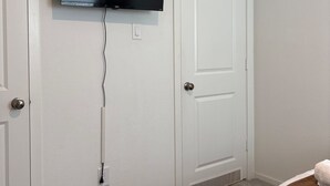 Una camera da letto con televisione a parete, una porta e pavimento coperto di moquette.