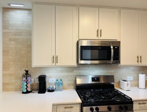 A modern kitchen with stainless steel appliances, including a microwave and stove, light-colored cabinets, and a coffee maker. - New Home in New Community Near Downtown Houston (Houston)