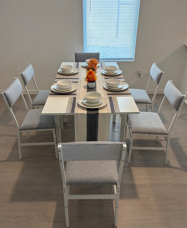A dining area with a table set for eight, surrounded by chairs, a window with blinds, and a small vase with flowers. - New Home in New Community Near Downtown Houston (Houston)