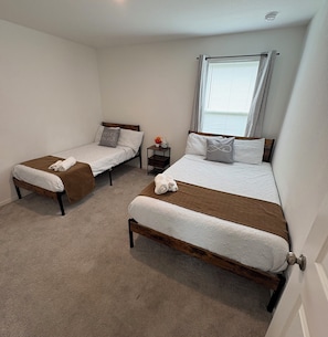 A bedroom with two single beds, a nightstand with a vase, and a window with blinds. - New Home in New Community Near Downtown Houston (Houston)