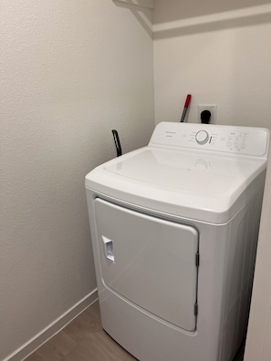 A white front-loading washer and dryer in a corner of a room with a textured white wall and wooden flooring. - New Home in New Community Near Downtown Houston (Houston)