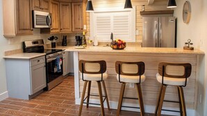 A kitchen with wooden cabinets, stainless steel appliances, a central island with bar stools, and pendant lighting.