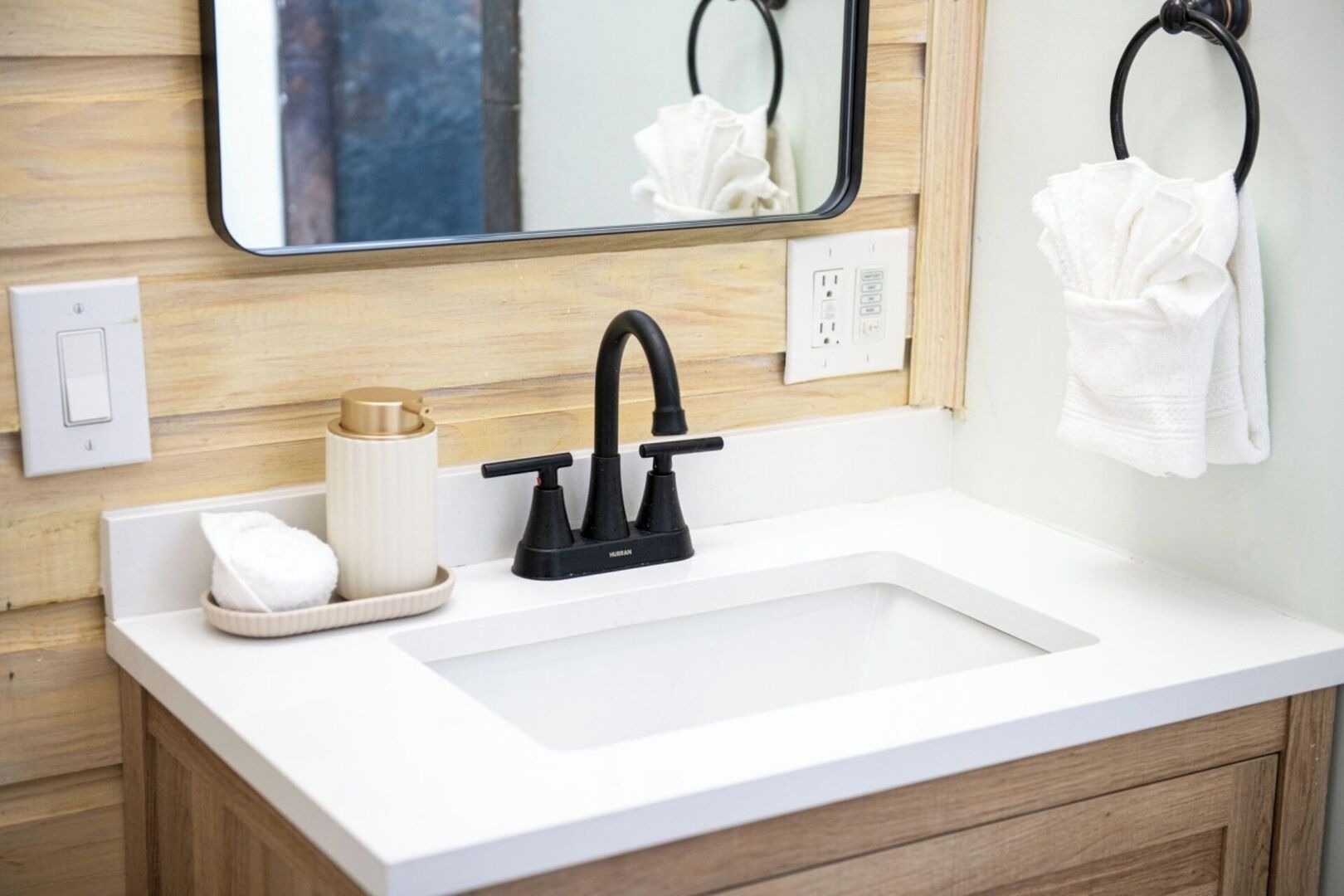 Un baño con un lavamanos blanco, grifo negro y paneles de madera.