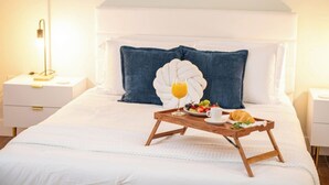 A neatly made bed with a tray of breakfast items, including fruit and juice, in a well-lit room with a modern design.