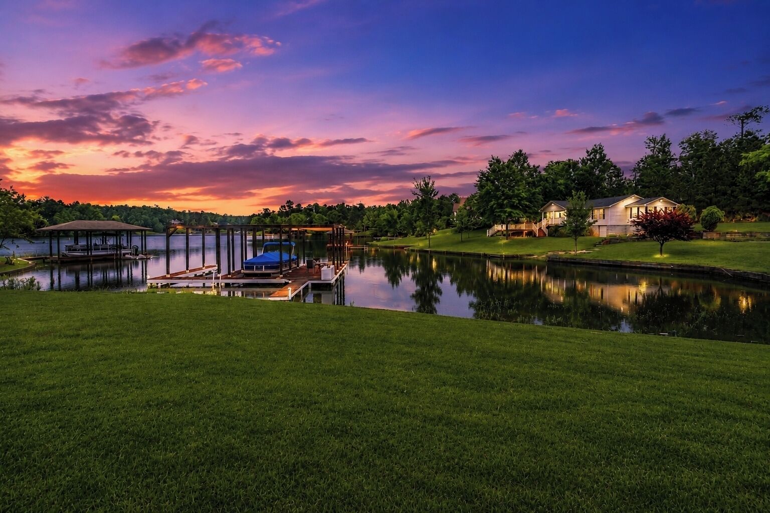 A lakeside property with a dock, a covered seating area, and a well-maintained lawn.