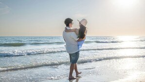 A couple embracing on a beach with the ocean and a clear sky in the background. - Steps to Beach, Heated Pool, Boutique Queen Studio (Madeira Beach)