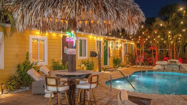 A poolside area with a thatched umbrella, a neon sign, and a pool. - Steps to Beach, Heated Pool, Boutique Queen Studio (Madeira Beach)