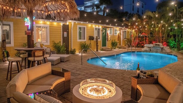 Un área junto a la piscina con una fogata, asientos exteriores y luces colgantes.
