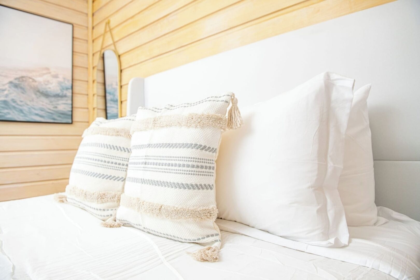 A bed with white bedding, two pillows with a striped pattern, and a wooden headboard.