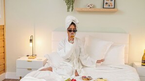 Un dormitorio con cama, mesitas de noche, una lámpara y un estante en la pared con objetos decorativos.
