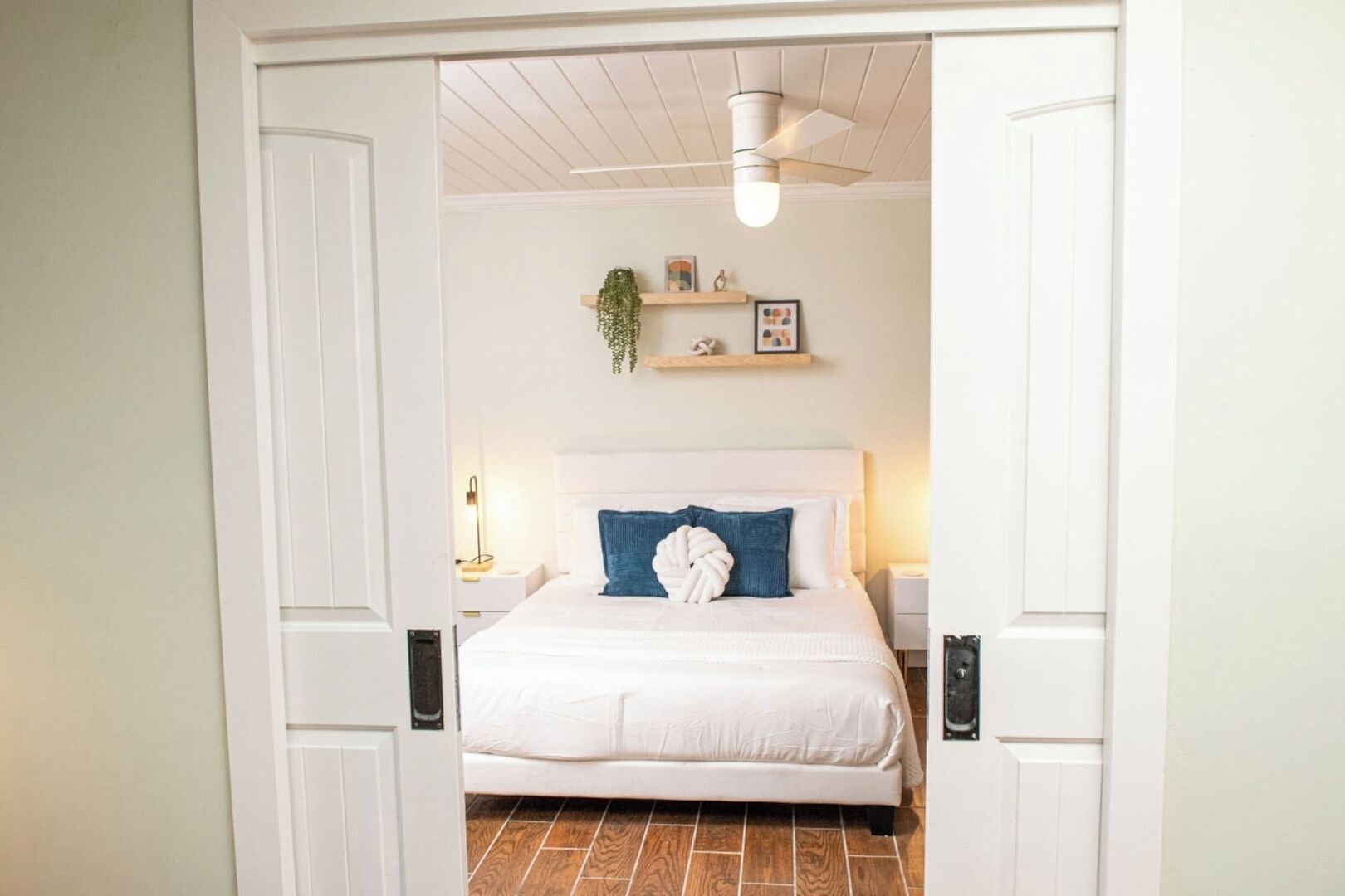 Een slaapkamer met een wit bed, een blauw kussen en een plafondventilator.