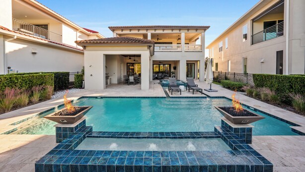 Un área de piscina moderna con jacuzzi, mobiliario exterior y un edificio de dos pisos al fondo.