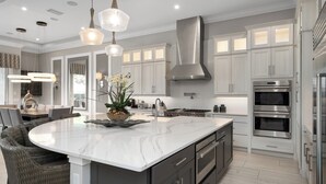 Una cocina moderna con una isla grande, electrodomésticos de acero inoxidable e iluminación colgante.