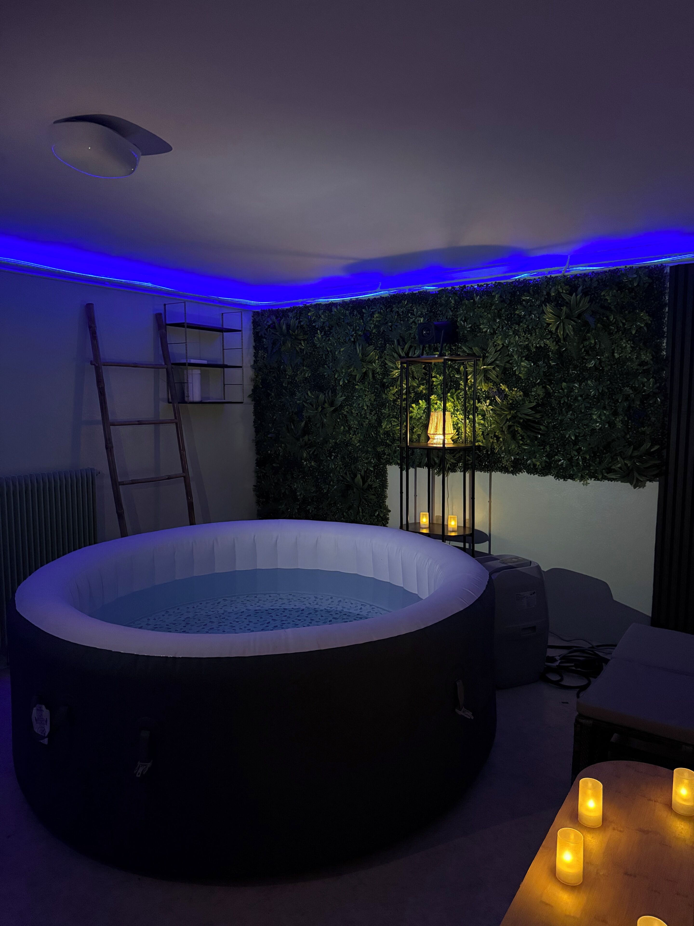 Ein Zimmer mit einer runden Whirlwanne, einem Wandregal, einer Leiter und einem kleinen Tisch mit Kerzen.