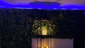 A room with a white circular seating area, a wall with dense foliage, and a table with a lamp. - Modern house by the sea (Arès)