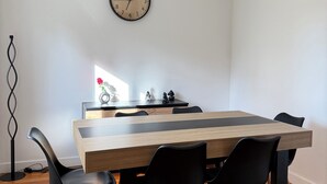 A dining area with a wooden table, black chairs, a wall clock, and a ceiling track lighting system. - Modern house by the sea (Arès)