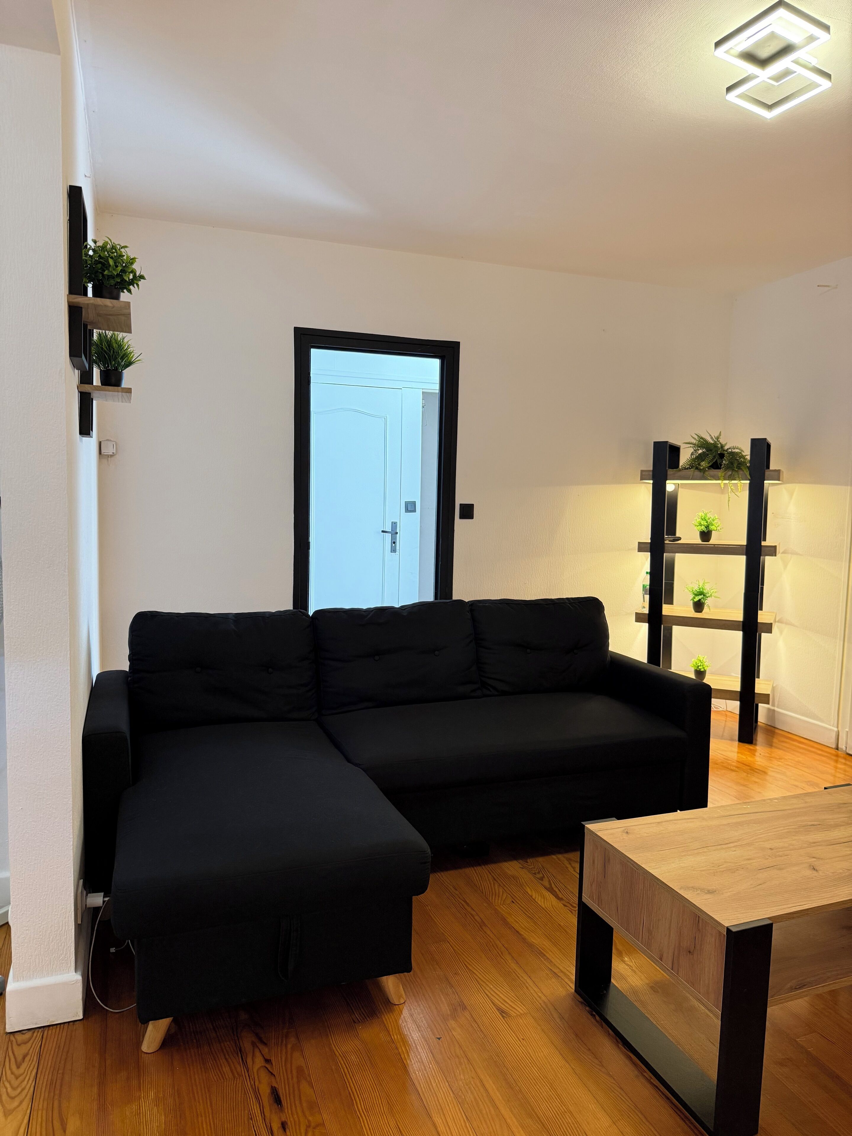 Un salon moderne avec un canapé d’angle, une table basse en bois et une étagère intégrée agrémentée de plantes.