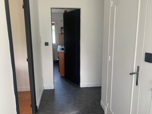En hall med mörkt golv, vita väggar och en delvis öppen dörr som leder till ett köksområde.