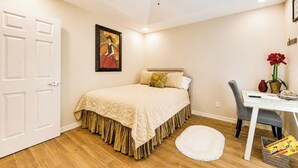 A bedroom with a bed, a desk, a chair, a ceiling fan, and a painting on the wall.