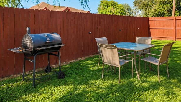 A backyard with a barbecue grill, a table, and chairs.
